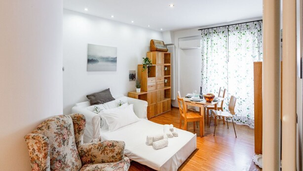 A modern room with a bed, a wooden cabinet, a dining table with chairs, and a window with curtains. - GuestHost - Ponte Solferino Bright & Cozy APT (Pisa)