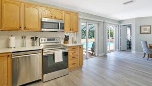 A spacious kitchen with wooden cabinets, stainless steel appliances, and a view to a backyard with a pool. - Casa Boca - Perfect Florida Getaway with Large Heated Saltwater Pool (Boca Raton)