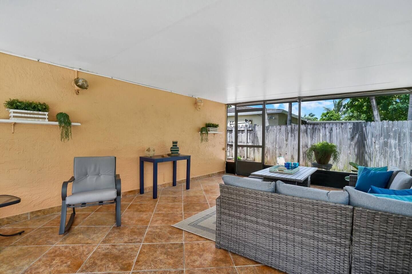 A covered patio with a grey sofa, a grey armchair, and a small table with decorative items.