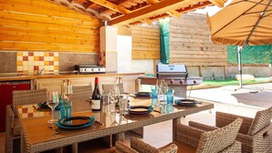 Une cuisine extérieure équipée d’un barbecue, d’une table à manger avec des chaises et d’un parasol pour la terrasse.