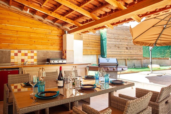 An outdoor kitchen with a grill, dining table with chairs, and a patio umbrella.