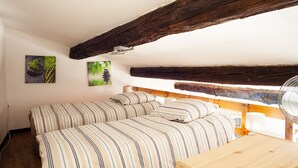 Une chambre avec deux lits, des poutres en bois, un ventilateur et des œuvres d’art murales.