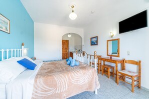 A bedroom with a bed, a desk, a chair, a TV, and a bathroom visible through an archway.