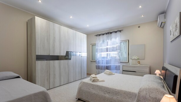 A modern bedroom with two beds, a wardrobe, a vanity with a mirror, and a bedside lamp.