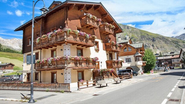 A wooden building with balconies, a street, and mountains in the background. - 'Chalet Letizia Apartment Bilo' with Mountain View, Balcony & Wi-Fi (Livigno)