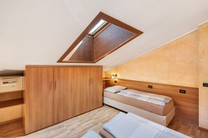 A compact bedroom with a sloped ceiling, a wooden wardrobe, a bed with white bedding, and a small bedside table.