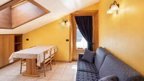 A room with a dining table, sofa, wooden ceiling, and a wall-mounted light fixture. - 'Chalet Letizia Apartment Bilo' with Mountain View, Balcony & Wi-Fi (Livigno)