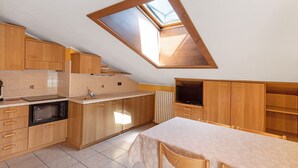 A compact kitchen with wooden cabinets, a microwave, a table with chairs, and a skylight. - 'Chalet Letizia Apartment Bilo' with Mountain View, Balcony & Wi-Fi (Livigno)