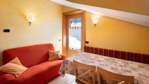 A room with a red sofa, a table with a patterned tablecloth, and two wall-mounted light fixtures. - 'Chalet Letizia Apartments Trilo' with Mountain View, Balconies & Wi-Fi (Livigno)