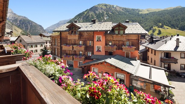 A hotel with a wooden facade, balconies with plants, and a mountain backdrop. - 'Chalet Letizia Apartments Trilo' with Mountain View, Balconies & Wi-Fi (Livigno)