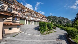 A multi-story hotel with balconies, a parking area, and a mountainous backdrop. - Apartment 'with Stunning Views' and Balcony (Tremosine)