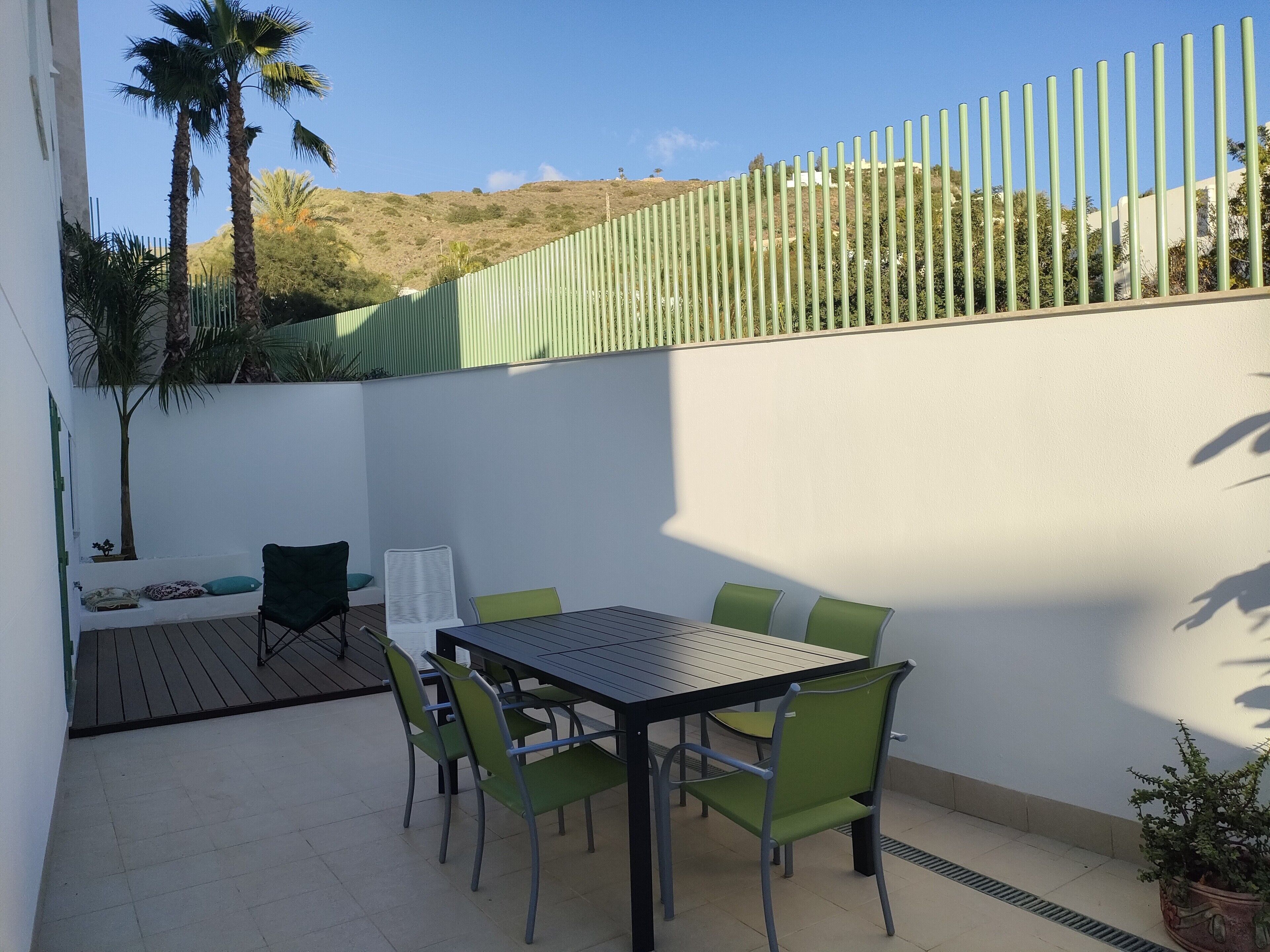 A patio with a table and chairs, a small seating area, and a view of a hilly landscape.