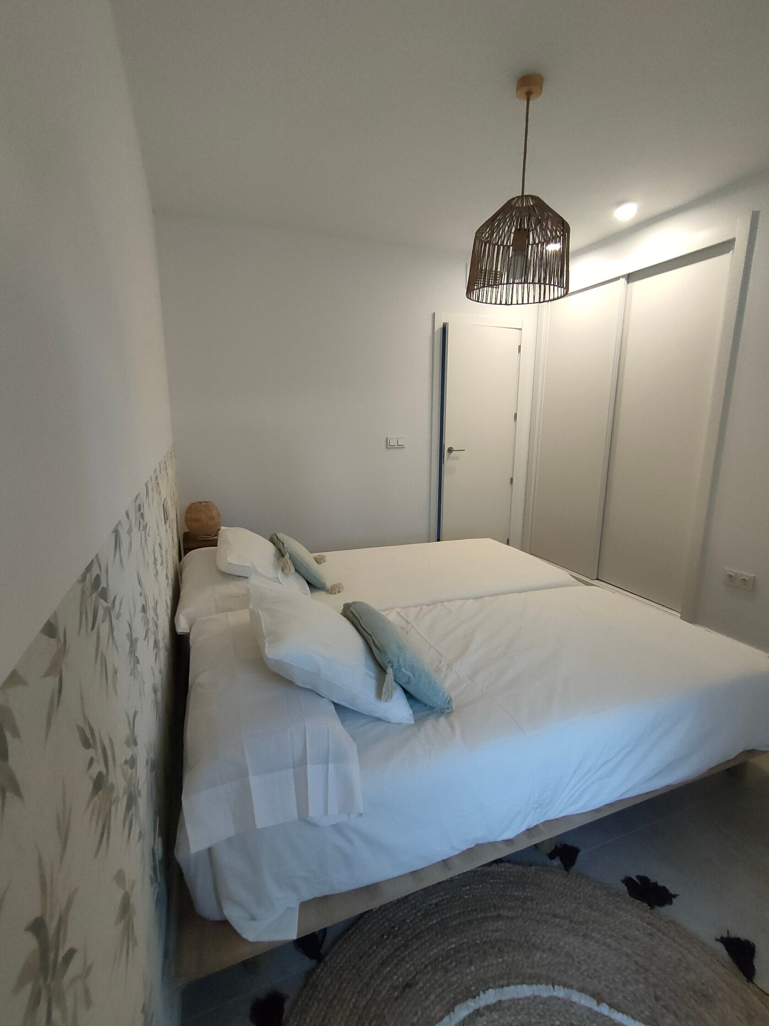 Een slaapkamer met een bed, nachtkastje, hanglamp en een kledingkast.