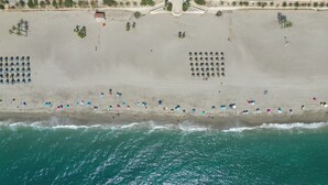Une vue aérienne d’une plage avec des rangées de parasols et de chaises de plage, une tour de surveillance et un petit bâtiment.