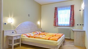 A bedroom with a wooden bed, bedside tables, a radiator, and a window with curtains. - Apartment 'Aronne Bait Giobbe' with Mountain View, Garden & Wi-Fi (Livigno)