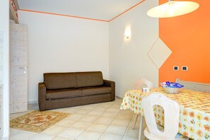 Ein Zimmer mit einer Couch, einem Tisch mit Blumenmuster-Tischdecke, einer Wandleuchte und einem Teppich mit Muster.