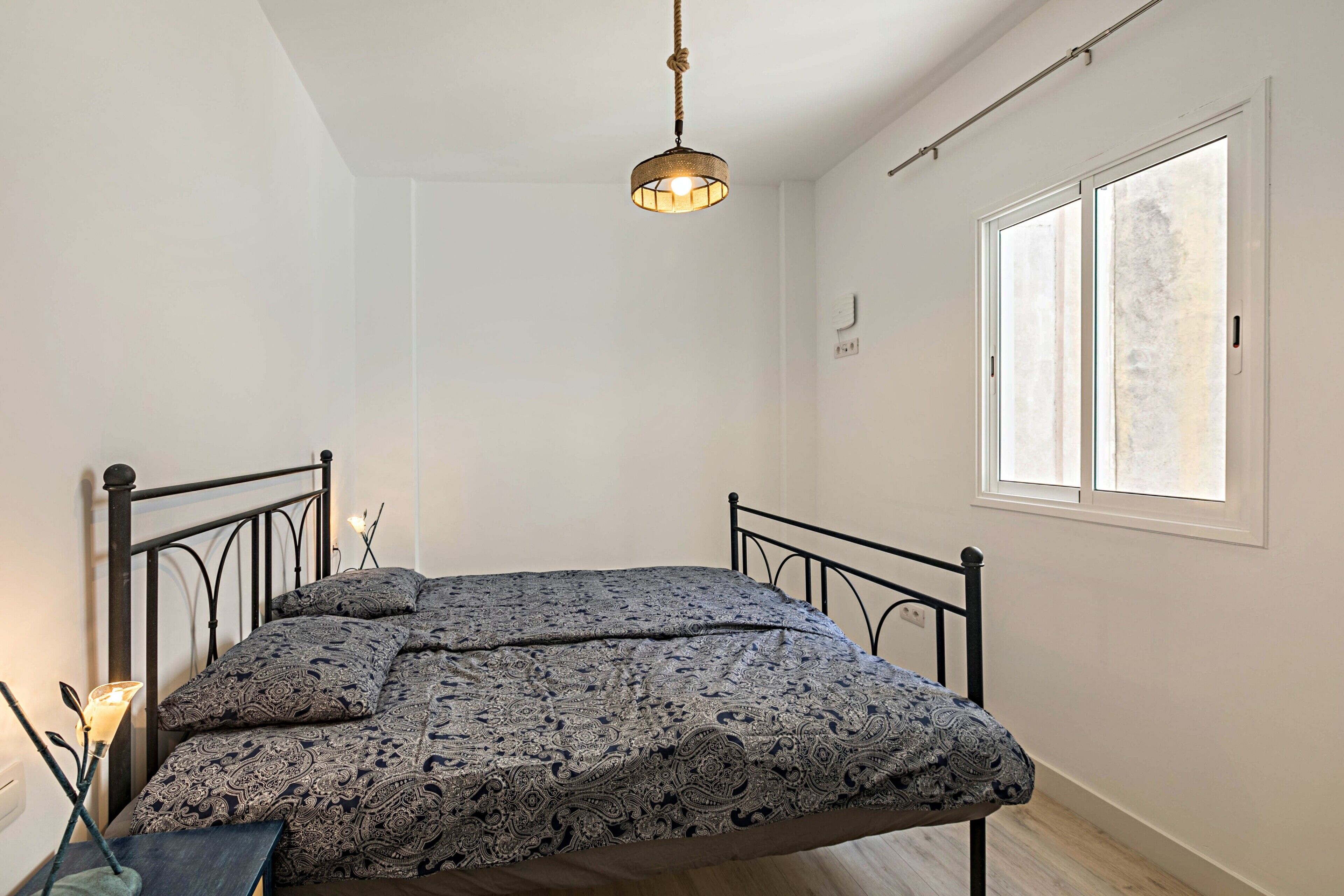A bedroom with a bed, a window, and a hanging light fixture.