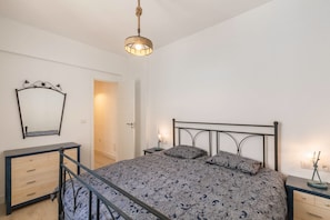 A bedroom with a bed, bedside tables, a dresser, a mirror, and a hanging light fixture.