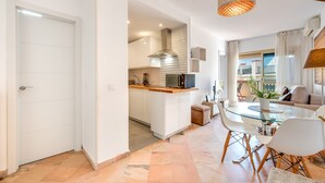 A modern kitchen with white cabinets, a glass dining table, and a hanging light fixture. - ‘Romana Playa’ Apartment with Pool, Wi-Fi & Air Conditioning (Marbella)