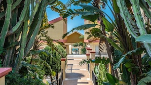 A pathway leading to a building with a red roof, surrounded by lush tropical plants. - ‘Romana Playa’ Apartment with Pool, Wi-Fi & Air Conditioning (Marbella)