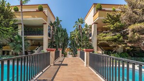 A poolside pathway leading to a building with balconies, surrounded by cacti and palm trees. - ‘Romana Playa’ Apartment with Pool, Wi-Fi & Air Conditioning (Marbella)