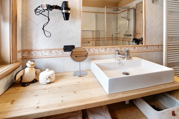 Un baño con tocador de madera, un espejo grande, un lavabo blanco y zona de ducha.