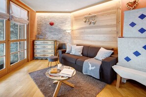 A cozy living room with a sofa, a small table, a dresser, and a stone wall.