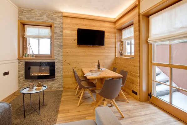 Une pièce chaleureuse avec un décor intérieur en bois, une cheminée, un téléviseur fixé au mur et une table à manger avec des chaises.