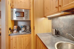 A compact kitchen with wooden cabinets, a stainless steel sink, a microwave, a coffee maker, and a toaster.