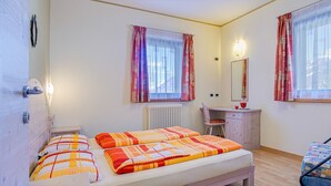 Ein Schlafzimmer mit einem Bett, einem Schreibtisch, einem Stuhl und einem Fenster mit Vorhängen.