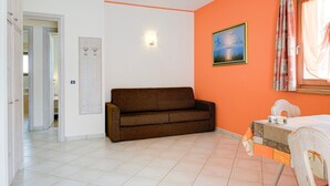 Ein Zimmer mit braunem Sofa, einem Bett mit gemustertem Überwurf, einem Bild an der Wand und einem Fenster mit Vorhängen.