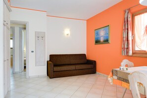 Une pièce avec un canapé marron, un lit recouvert d’une couvre-lit à motifs, un tableau au mur et une fenêtre avec des rideaux.