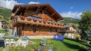 Eine Holzhütte mit Balkonen, Sitzgelegenheiten im Freien und einer Bergkulisse.