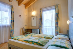 Een slaapkamer met twee bedden, een bureau, een stoel, een spiegel en een raam met gordijnen.