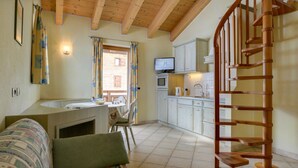 Een gezellige kamer met een houten plafond, een bank, een eettafel, een keuken met kastjes, een televisie en een houten wenteltrap.