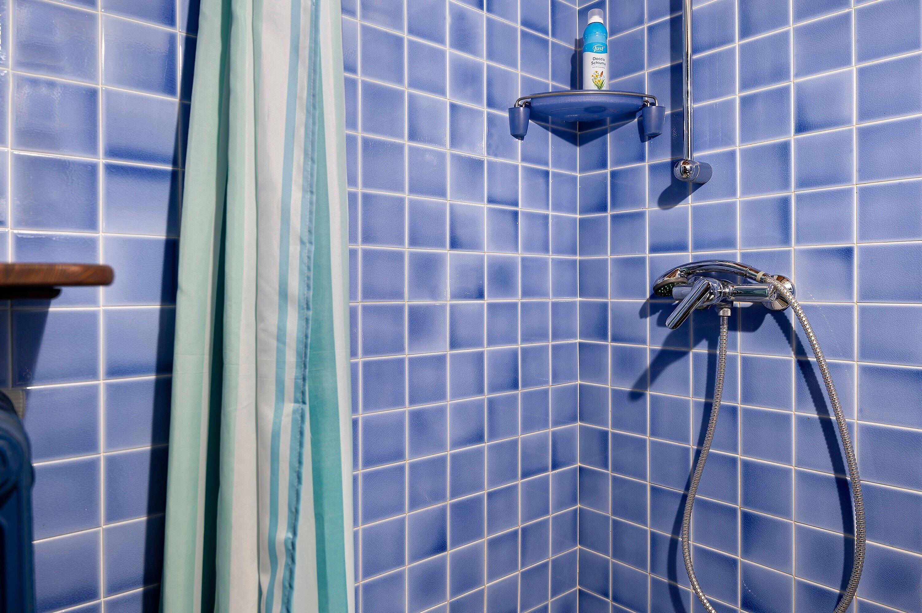 Een badkamer met blauwe betegelde wanden, een douchekop en een zeepdispenser.