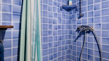Een badkamer met blauwe betegelde wanden, een douchekop en een zeepdispenser.