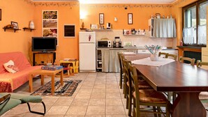 A compact living space with a sofa, TV, dining table, chairs, kitchen area, and a window.
