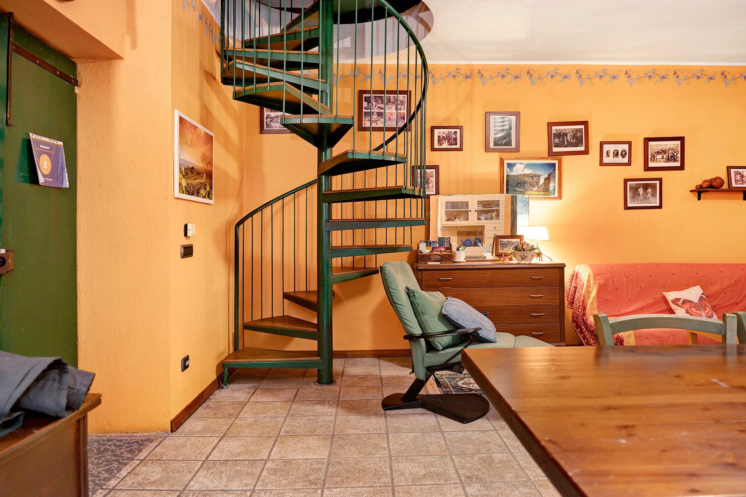 Une pièce avec un escalier en colimaçon, une table à manger, une chaise verte, un meuble en bois et un canapé rouge.
