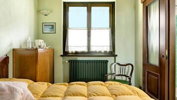 A bedroom with a bed, a wooden wardrobe, a chair, a radiator, and a window with a lace curtain.
