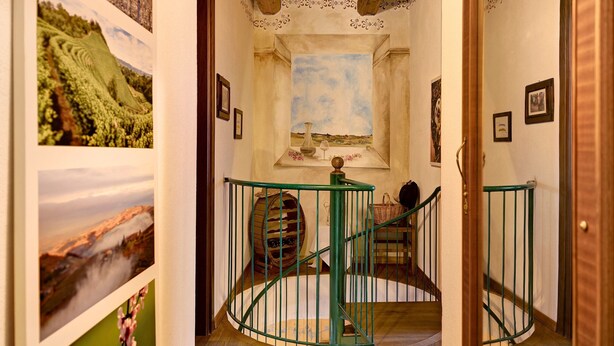 A spiral staircase with green railings, a rustic wooden floor, and a small window with a landscape painting.