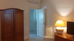 A hallway with a wooden door, an air conditioning unit, a white door, and a table with a lamp.