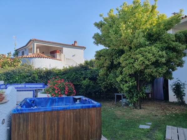 A residential backyard with a swimming pool, a large tree, and a house with a tiled roof.