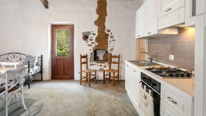 A rustic kitchen with a stone wall, wooden chairs, a dining table, and a stove. - Holiday Home 'Stazzu Saiacciu' with Terrace (Palau)