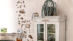 A stone wall, a wooden chair, a cabinet with glass doors, and a small table with a pitcher and a picture frame. - Holiday Home 'Stazzu Saiacciu' with Terrace (Palau)