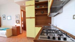 Een keuken met een gasfornuis, houten keukenkastjes en een betegelde vloer.
