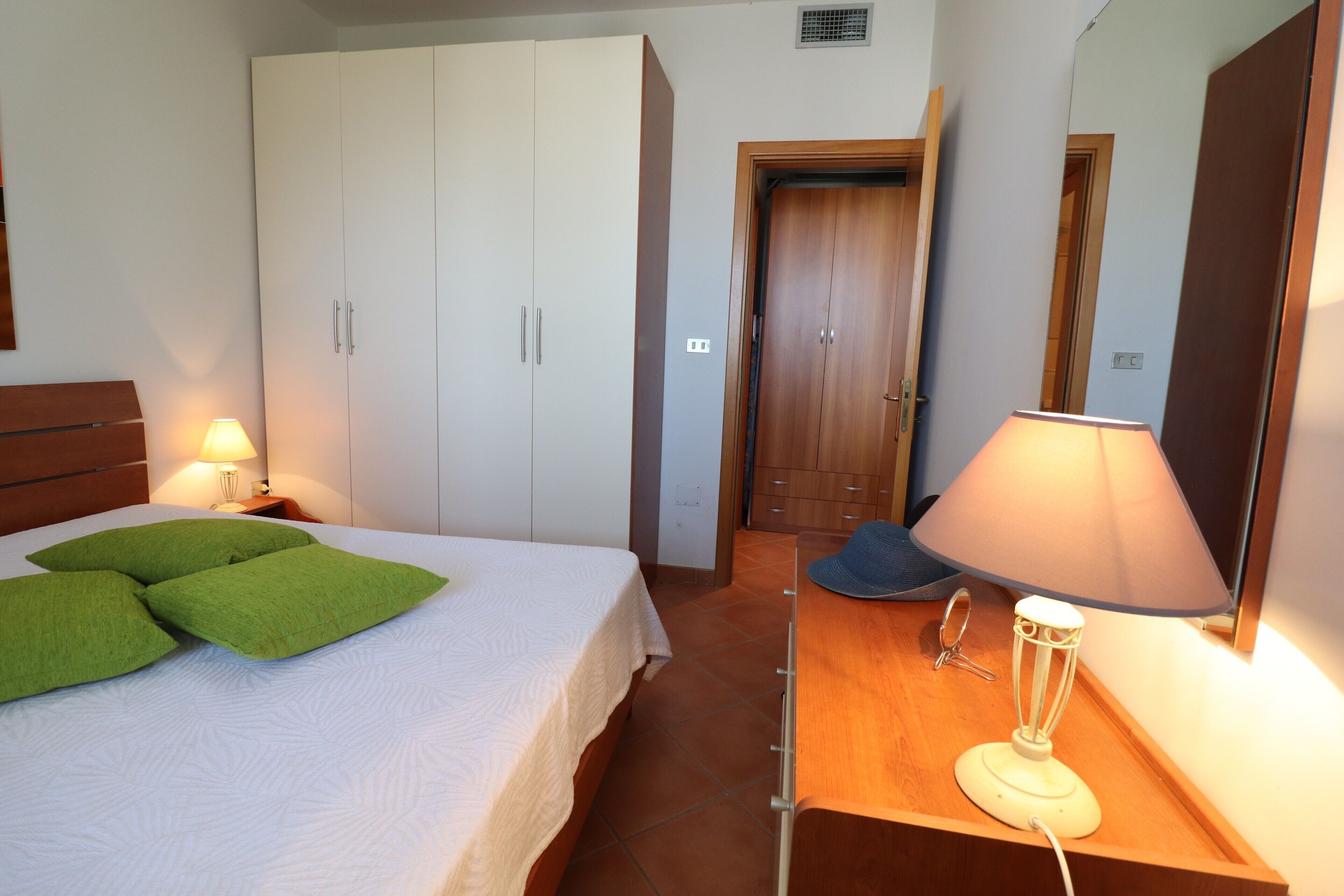 Camera da letto con un letto, un comodino, una lampada, un settimino in legno e una porta.