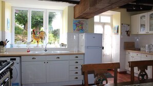 A kitchen with white cabinets, a sink, a stove, and a refrigerator. There is a window with a rooster outside. - Gite La Maison du Passeur (Availles-Limouzine)