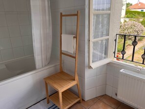 A corner bathroom with a wooden chair, a window with a view of a garden, and a radiator. - Gite La Maison du Passeur (Availles-Limouzine)