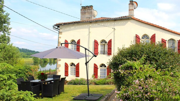 A large house with a garden, a dining table with chairs, and a patio umbrella. - Gite La Maison du Passeur (Availles-Limouzine)